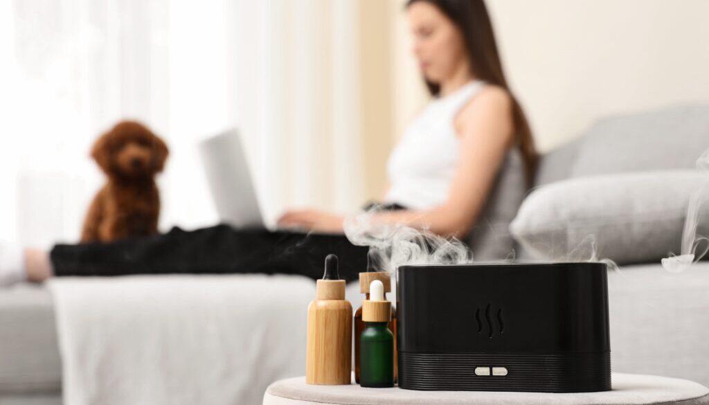 Aromatherapy diffuser with essential oils and a woman working on a laptop with a dog in the background, Aromatherapy diffuser with essential oil bottles on a side table, creating a relaxing atmosphere